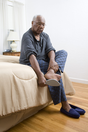 Hombre sentado en el borde de la cama mirándose la planta del pie con un espejo.