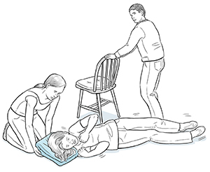Una mujer coloca una almohada debajo de la cabeza de una mujer que tiene una convulsión, mientras un hombre quita una silla de en medio.